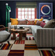 JJapura Green upholstery on the corner sofa creates a striking horizontal division, with bold graphic patterns in green, blue, and orange bringing life to the space. The rich dark walls act as a backdrop, highlighting the vibrant colours and creating a contemporary, effortlessly curated atmosphere.
